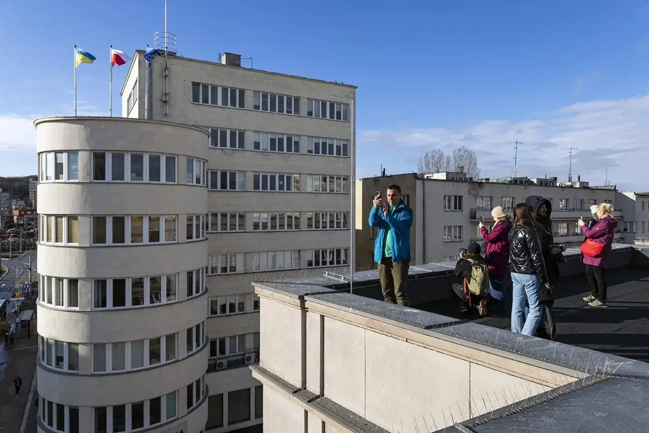 Grupa turystów podziwia architekturę modernizmu w Gdyni, robiąc zdjęcia charakterystycznego budynku z zaokrąglonymi narożnikami.