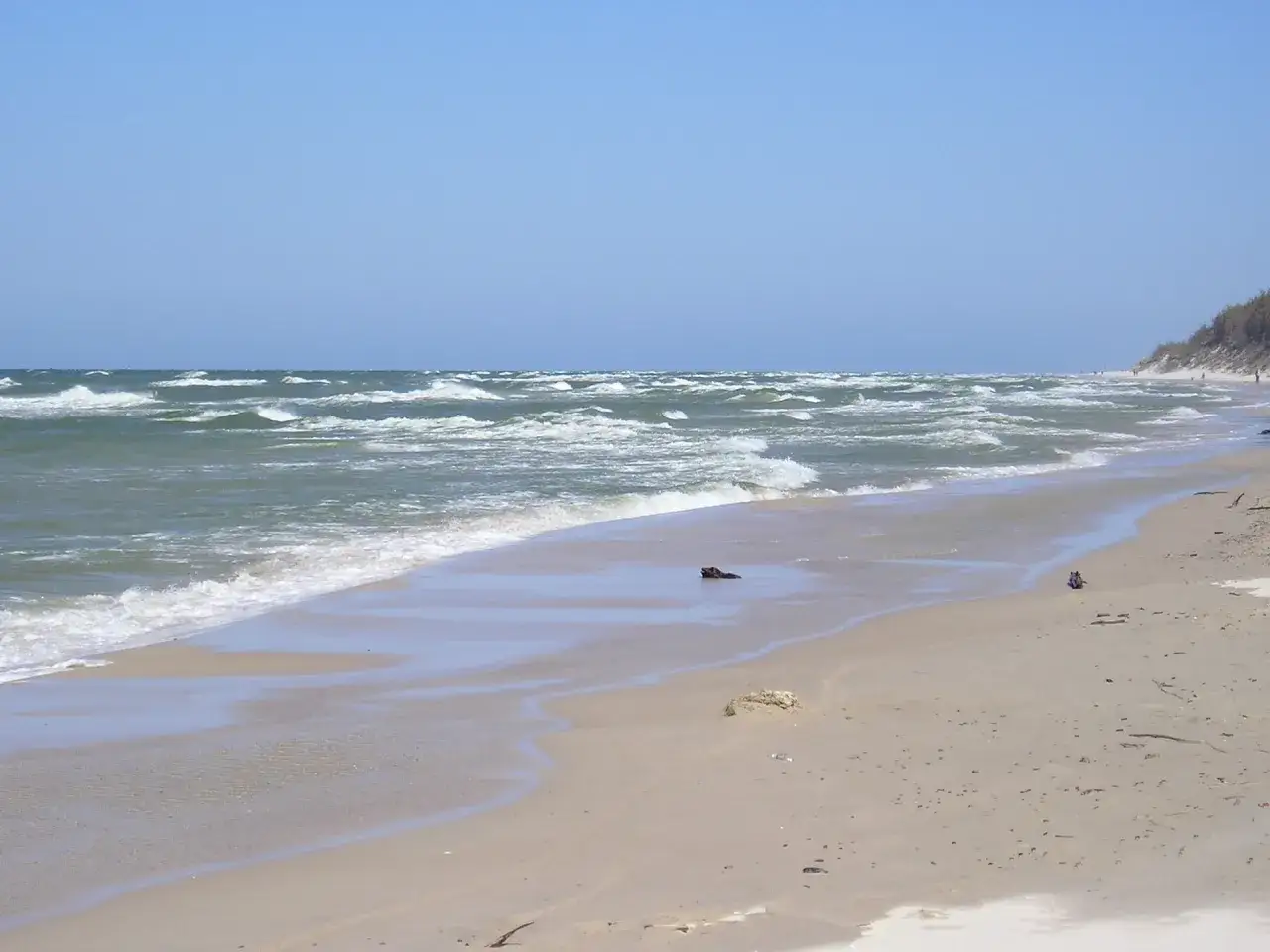 Plaża z falami i wydmami. W oddali widać ludzi spacerujących, co sugeruje, że to miejsce oferuje ciekawe rowy atrakcje.