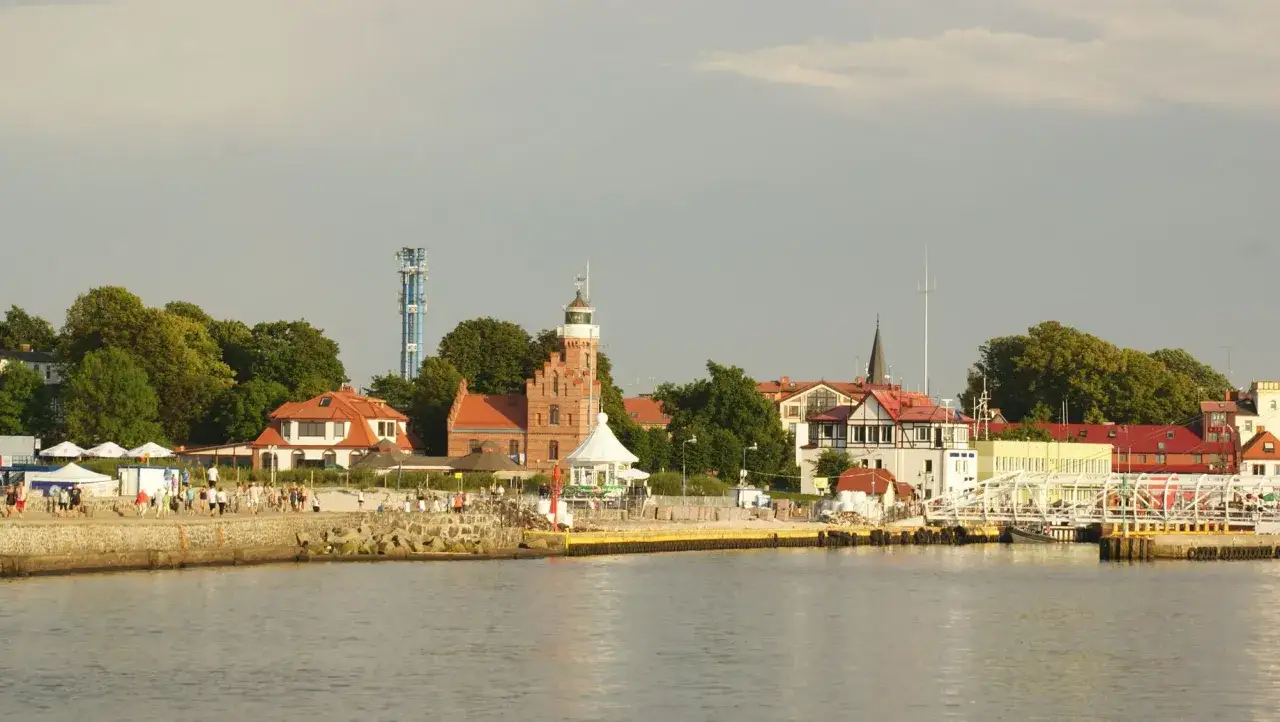Urokliwy widok na port w Ustce. Latarnia morska, biały most i promenada z spacerującymi ludźmi to miejsca, które warto zobaczyć.