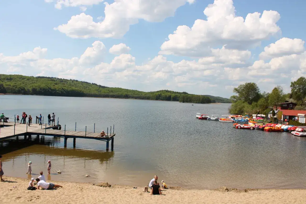Słoneczny dzień w ostrzyce park. Ludzie odpoczywają na plaży, spacerują po molo i pływają kolorowymi łódkami.