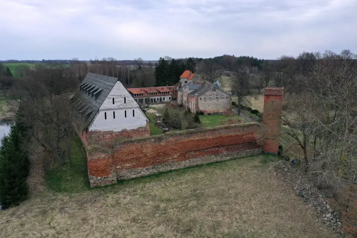 Zamek Kiszewski, z ceglanymi murami i wieżą, otoczony zielenią i drzewami.