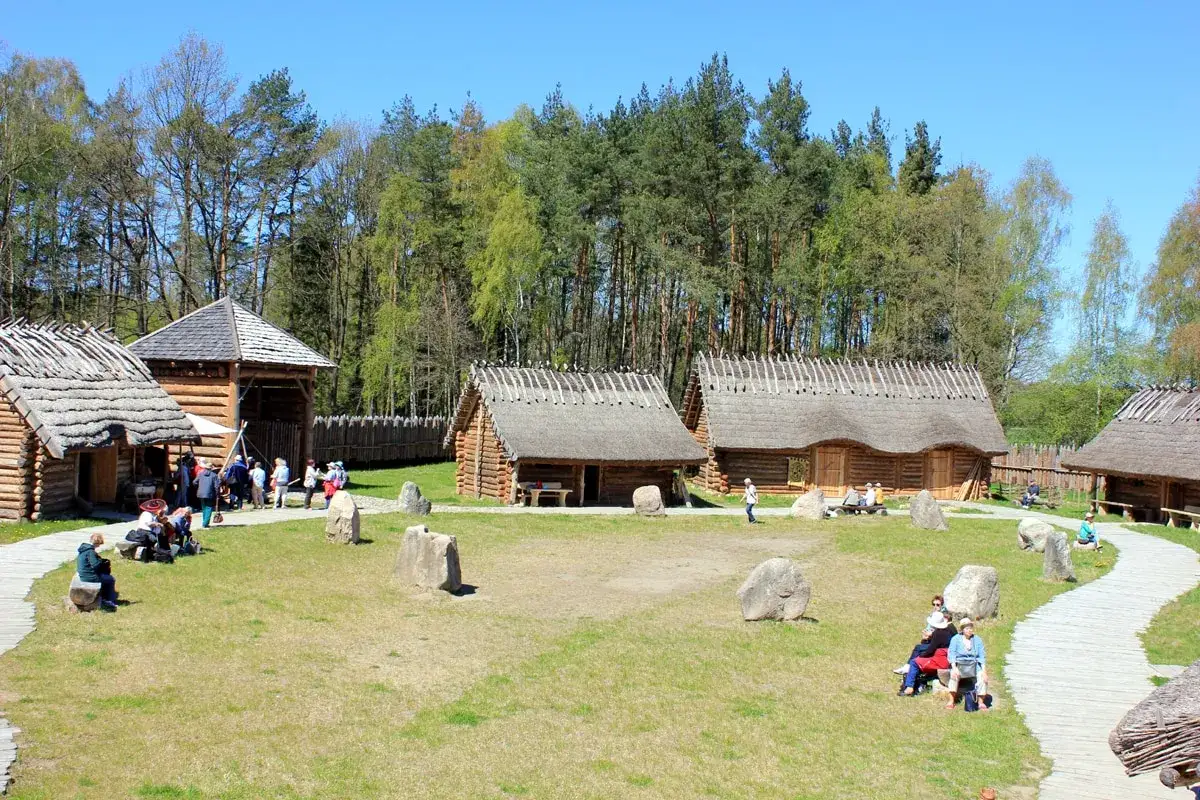 Odwiedzający zwiedzają osadę sławutowo, podziwiając drewniane chaty kryte strzechą i otaczający las.