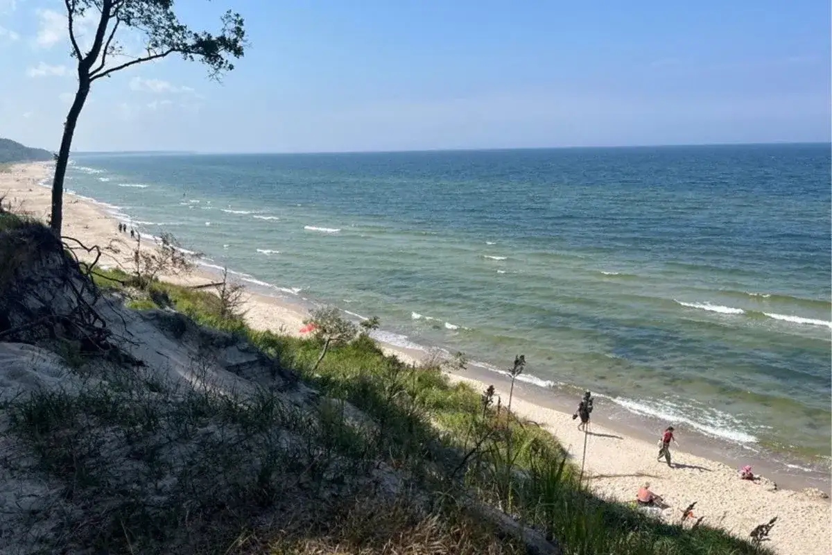 Piękne plaże nad morzem, z piaszczystym wybrzeżem i łagodnymi falami. Kilka os&oacute;b spaceruje i odpoczywa na piasku.