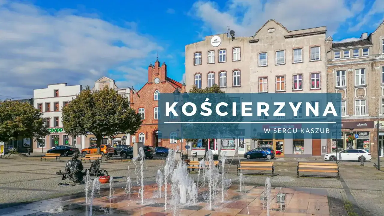 Kościerzyna rynek z fontanną i ławkami, w tle kamienice i wieża zegarowa.