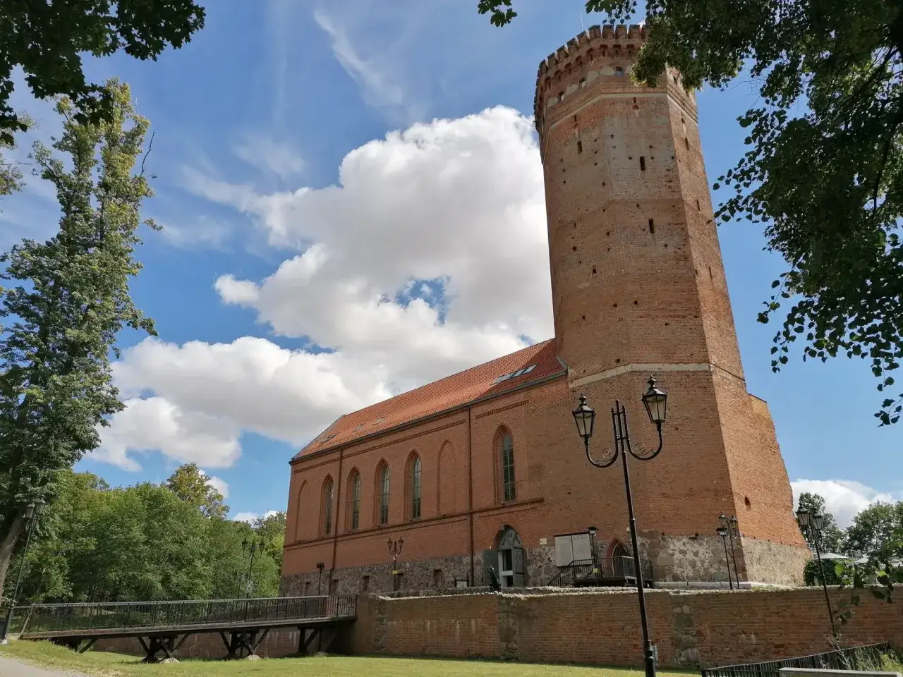Chojnice zamek krzyżacki, ceglana wieża i budynek muzeum pod błękitnym niebem z chmurami.