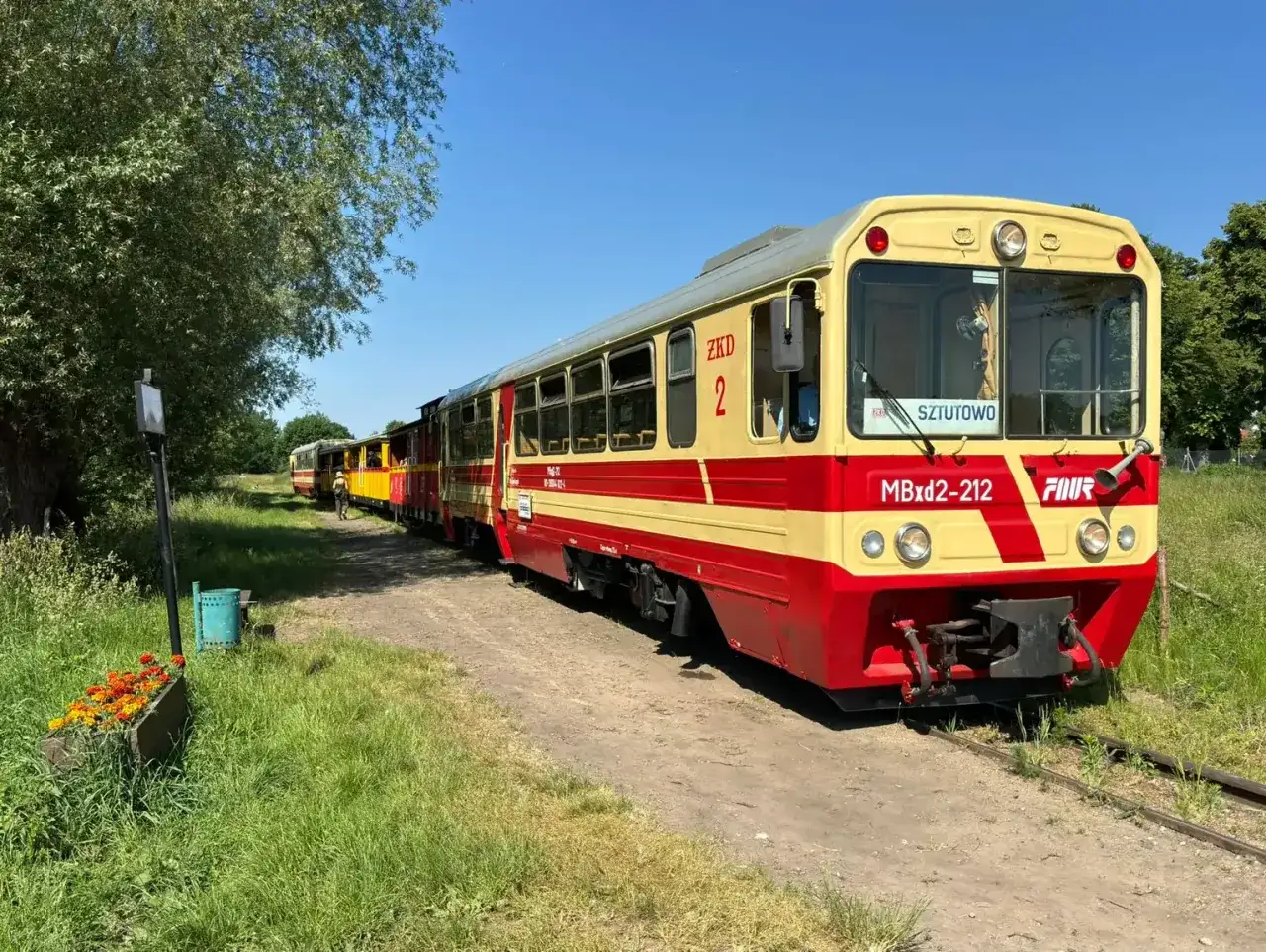 Kolej wąskotorowa Jantar, z czerwono-żółtymi wagonami, czeka na pasażerów na słonecznej trasie.