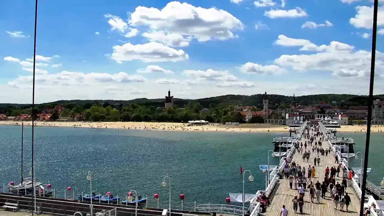 Tłum ludzi spaceruje po najdłuższym drewnianym molo w Sopocie, podziwiając błękitne morze i piaszczystą plażę.