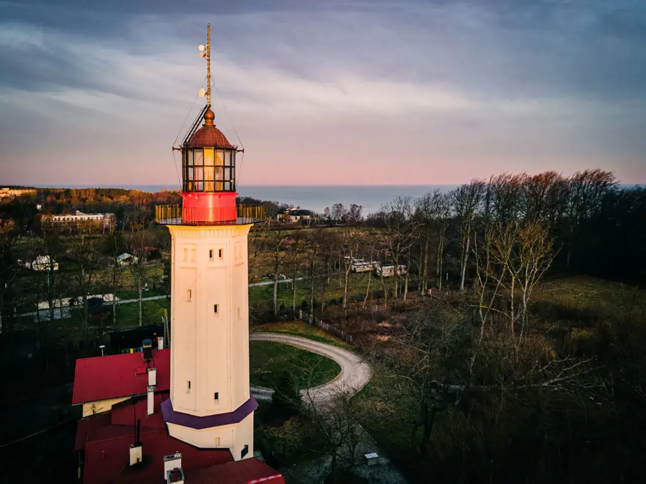 Latarnia morska na przylądku na pobrzeżu kaszubskim o zachodzie słońca. W tle morze i las.