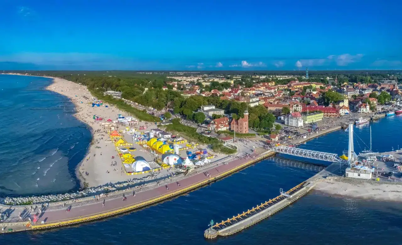 Tętniąca życiem ustka promenada z plażą, namiotami i miastem w tle.