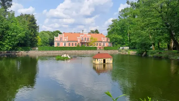 Wejherowo Park Majkowskiego: urokliwy staw z pływającym domkiem i łabędziami, w tle różowy pałacyk. Idealne miejsce na rodzinne imprezy.